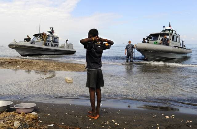 A Haitian boy watches as U.S. Sailors in rigid-hull inflatable boats from the amphibious dock landing ships USS Fort McHenry (LSD 43) and USS Carter Hall (LSD 50) arrive at the New Hope Mission in Bonel, Haiti on January 19, 2010. The multi-purpose amphibious assault ship USS Bataan (LHD 5) is on station in Haiti in support of Operation Unified Response, a joint humanitarian assistance mission to Haiti following the 7.0-magnitude earthquake that struck the country on January 12.  WAX20100120701