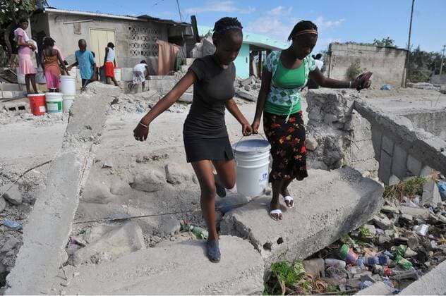 Two women carry a bucket of water into a refugee camp in Port-au-Prince, Haiti on January 27, 2010. Haiti continues to suffer after a 7.0 magnitude earthquake devastated the country on January 12.  HAI20100127301
