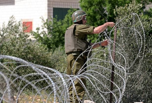 (100312)-- BETHLEHEM, March 12, 2010 (Xinhua) -- An Israeli soldier adjusts a wire fence during a demonstration by Palestinians and international peace activists against the Israeli separation wall in the West Bank village of Al-Maasara, near Bethlehem, on March 12, 2010. (Xinhua Luay Sababa) (lyi) (3)BETHLEHEM-ISRAEL-DEMONSTRATION 