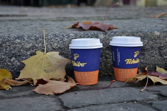 Tchibo-Kaffeebecher am Straßenrand neben Laub