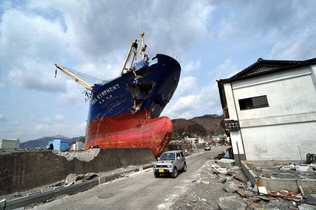 April 1st, 2011, Kamaishi, Japan - A small van goes by the looming bow of Asia Symphony, a Panamanian ocean going vessel being left aground on the wharf in the port of Kamaishi , Iwate Prefecture, on April 1, 2011, three weeks after this major northeastern Japanese port was destroyed by a magnitude 9.0 earthquake and ensuing tsunami.  (ayfa004588)