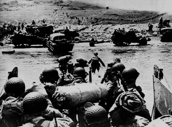 IMAGO History, Zweiter Weltkrieg: 1939 - 1945 WW2: D Day. American shock troops move from a landing craft through the shallow water onto a beach-head in Northern France during the allied landings. Half-tracks and a beached DUKW on the beach-head. The smoke in the background is from naval gunfire supporting the attack. 6th June 1944. Mono Print !AUFNAHMEDATUM GESCHÄTZT! UnitedArchives0782739