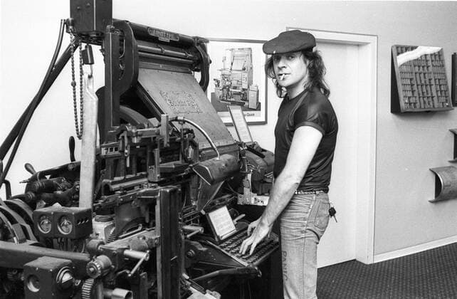 Udo Lindenberg (Rocksänger) 09 81 teu Mann Sänger Gesang Musik Rock Pop Musiker dunkelhaarig langhaarig leger T-Shirt dunkel Mütze Kappe Käppi glänzend stehend vor alter Linotype-Setzmaschine alt halb quer fragend lächelnd sich umdrehend zum Betrachter posierend Finger auf der Tastatur auf den Tasten schreibend Zigarette im Mund Fototermin Udo Lindenberg beim WB am 10.09.1981 SW-Negativ