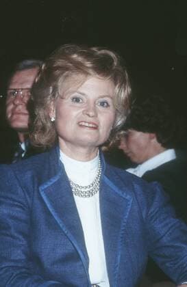 Hannelore Kohl (Ehefrau des Bundeskanzlers) 11 86 - Frau Gesellschaft Politik dunkelhaarig kurzhaarig Locken Schmuck Ohrring Kette seriös Jacke Blazer blau Bluse weiss sitzend Saal Halle dunkel halb hoch lächelnd