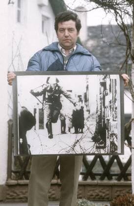 Conrad Schumann (Ex-DDR-Volkspolizist) 03 86 ru Ex-DDR-Volkspolizist Conrad Schumann im März 1986 mit dem Foto seiner Flucht vom 15. August 1961, fotografiert von Peter Leibing Deutschland deutsch Deutscher Deutsche Mann Einheit deutsche DDR Deutsche Demokratische Republik Hauptstadt geteilt geteilte Stadt Ostberlin Berlin Ost Sozialismus VoPo Mauerflüchtling Flüchtling Soldat Polizist ehemalig ehemaliger geflüchtet Foto historisch historisches Kalter Krieg Mauerbau Flucht am 15. August 1961 german former gdr policeman wall germany hoch halb stehend draußen zeigend exklusiv exklusiver Fototermin