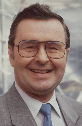 Ernst H. Hilbich (Schauspieler) 08 87 hör Mann Schauspiel Theater TV Fernsehen Komik dunkelhaarig kurzhaarig Brille seriös Jackett grau Hemd weiss Krawatte stehend draussen Portrait hoch lächelnd
