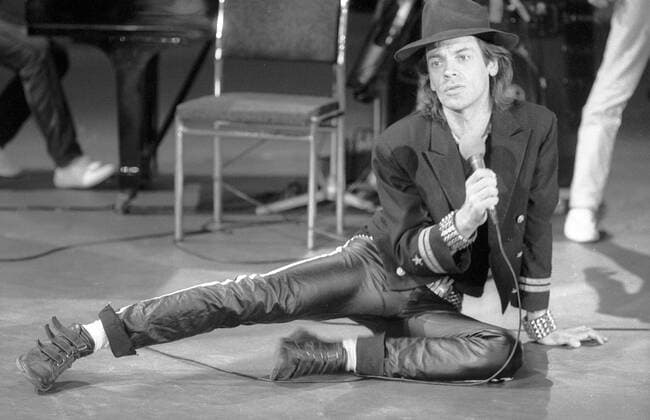 Udo Lindenberg (Rocksänger) 09 83 vZ Udo Lindenberg in der Fernsehsendung Tele-Illustrierte (ZDF) im September 1985 Deutschland deutsch Deutscher Mann Pop Rock Musik Gesang Sänger Musiker Komponist Maler Künstler Schriftsteller Auftritt Konzert Gig german singer composer musician dunkelhaarig langhaarig Lederhose Hut Sakko Jackett quer ganz freistellbar sitzend posierend singend Mikrofon haltend sw