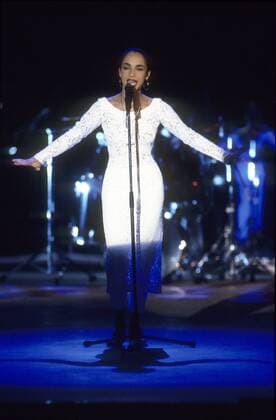 Sade (Sängerin) 11 88 - Sade Adu beim 1. Europäischen Filmpreis Felix am 26.11.1988 in Berlin Britin Großbritannien Nigeria Nigerianerin Frau Sängerin Gesang Musik Musikerin Pop Jazz Softjazz Fotomodell Model dunkelhaarig langhaarig Pferdeschwanz Schmuck Ohrringe Mikrofon Scheinwerfer Auftritt singend Konzert Bühne Kleid Hochformat hoch ganz stehend singend gestikulierend gestikulieren Gestik Helen Folasade Adu