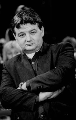 Joschka Fischer (Politiker) 01 91 pp Mann Politik Partei Die Grünen Bündnis 90 hoch Hochformat halb schwarzweiß sw Bundestag Bundesregierung Außenministerium Außenminister dunkelhaarig kurzhaarig sitzend seriös Anzug Jackett Hemd Fernsehsendung Studio Zuschauer neutral Mikrofon Mikrophon Mikro am Hemd Arme verschränkt nach unten schauend Armbanduhr Uhr In der Fernsehsendung Live im Januar 1991