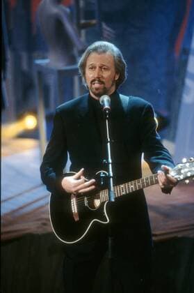 Bee Gees - Sänger - Barry Gibb - 02 97 her Musik Mann Gesang Pop Instrument Gitarre haltend spielend dunkelhaarig Bart seriös Jackettt schwarz Auftritt Bühne stehend Mikrophon singend halb hoch