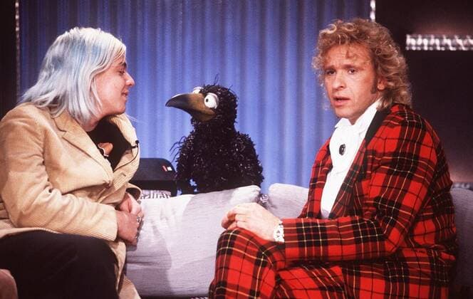 Thomas Gottschalk (re.); Nils Bokelberg mit Rudi in Kinder- Wetten, daß...? (ZDF) 12 96 rs TV Fernsehen Film Show Moderation Film Studio Dekoration Kulisse Mann Sofa sitzend Puppe Tier Rabe Beine Gespräch Bühne Auftritt Mikrophon BLUMENSTRAUß halb quer