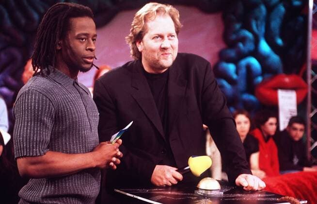 Dieter Gorny mit Mola Adebisi (li.) 04 98 pp Mann TV Fernsehen Popkomm VIVA TV Musik leger stehend Studio Dekoration Kulisse Tisch Mikrophon Zuschauer Publikum Gespräch halb quer