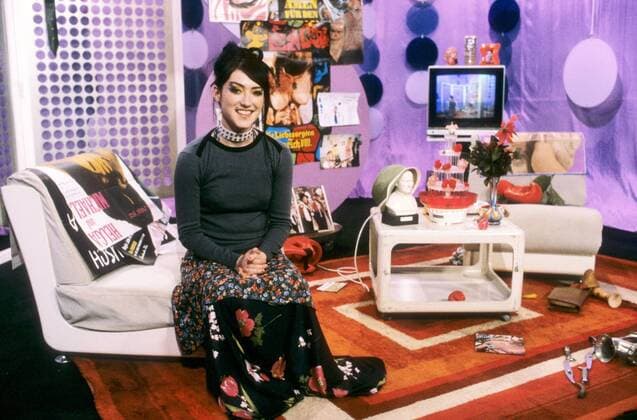 Charlotte Roche (TV-Moderatorin) 04 00 pp Frau Moderation TV Fernsehen VIVA Musiksender Sender Musik dunkelhaarig langhaarig Hochsteckfrisur Schmuck Armband Ring Lippenring Piercing Lippenpiercing leger Shirt grau Rock lang bunt gemustert geblümt Halsband sitzend aufstützend Sessel Kulisse Dekoration ganz quer lächelnd posierend Hände im Schoß gefaltet Fototermin Charlotte Roche am 20.04.2000 in Köln (exklusiv)