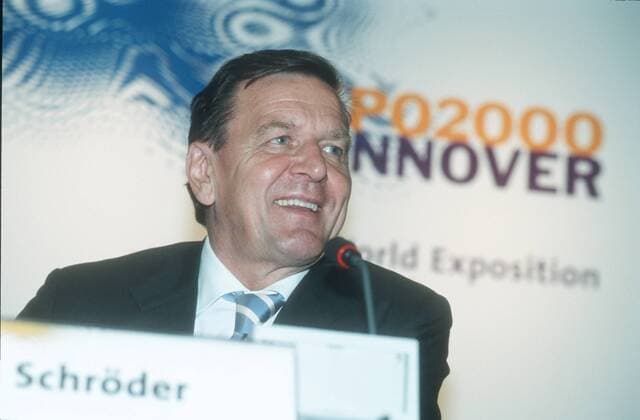 Gerhard Schröder (Bundeskanzler) 06 00 urb Mann Politik Partei SPD Bundeskanzler Kanzler Regierung Bundesregierung dunkelhaarig kurzhaarig seriös Jackett Hemd Krawatte sitzend Saal Halle dunkel Podium Pult Portrait quer lächelnd Froschperspektive Logo Schild Namensschild Mikrophon Fototermin EXPO-Eröffnung am 31.05. 01.06.2000 in Hannover