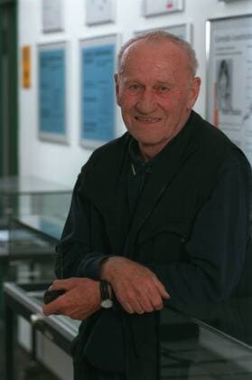 Max von der Grün (Schriftsteller) 07 02 thg Mann Autor Schriftstellerei Literatur Roman grauhaarig weißhaarig kurzhaarig Halbglatze leger Hemd Polohemd Weste stehend aufstützend Vitrine halb hoch lächelnd Pfeife haltend Fototermin Max von der Grün am 01.07.2002 in Paderborn