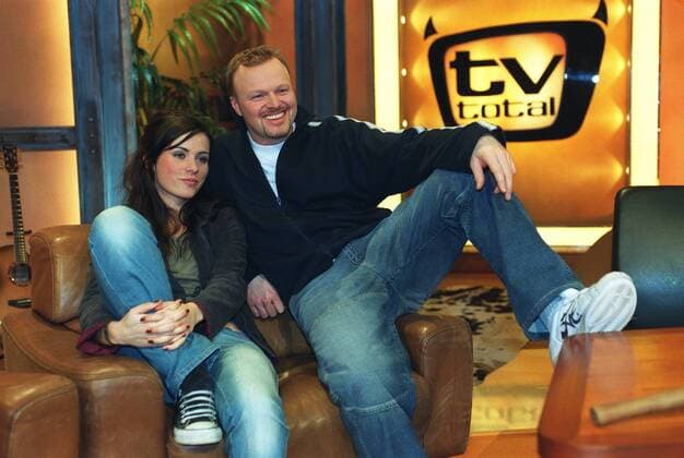 Stefan Raab mit Nora Tschirner in tv total (ProSieben) 01 03 pp Mann Moderator TV Fernsehen Moderation Musiker Musik Pop Gesang Sänger Produktion Unterhaltung Show dunkelhaarig kurzhaarig leger Trainingsjacke Sportjacke Shirt sitzend TV-Studio Kulisse Dekoration Logo halb quer sitzend lächelnd Sessel Fototermin tv total (ProSieben) am 06.01.2003 in Köln