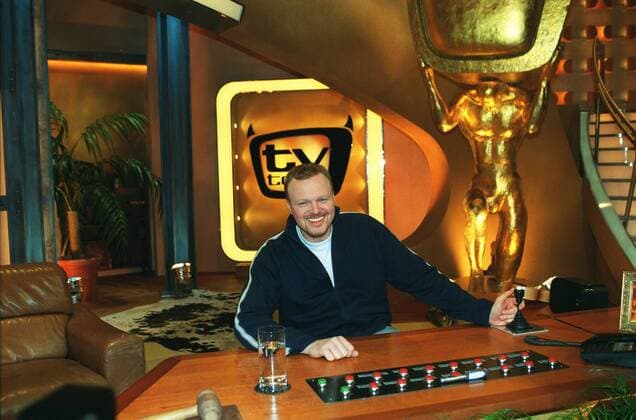 Stefan Raab in tv total (ProSieben) 01 03 pp Mann Moderator TV Fernsehen Moderation Musiker Musik Pop Gesang Sänger Produktion Unterhaltung Show dunkelhaarig kurzhaarig leger Trainingsjacke Sportjacke Shirt sitzend TV-Studio Kulisse Dekoration Logo halb quer sitzend lächelnd Tisch Moderationstisch Pult Glas Wasserglas Fototermin tv total (ProSieben) am 06.01.2003 in Köln