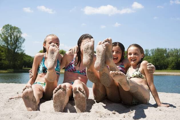 Freundinnen sitzen am Strand und strecken die sandigen Füße in die Kamera