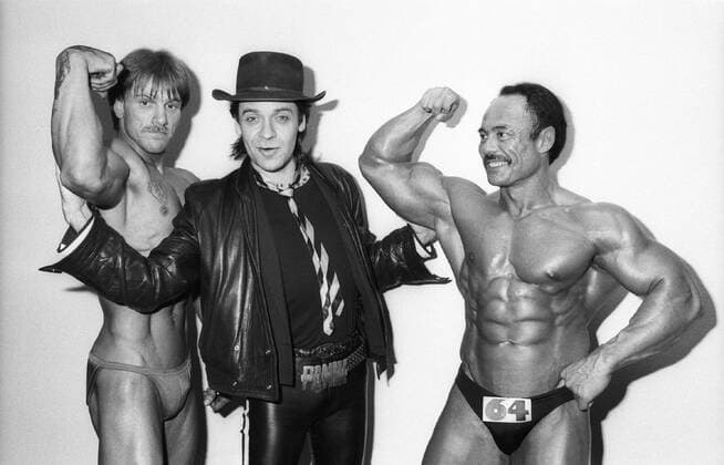 Udo Lindenberg (Mi.) (Musiker) 04 85 stroe Udo Lindenberg (Mitte) mit zwei Bodybuildern am 29. April 1985 am Rande von NDR2 Nonstop Deutschland deutsch Deutscher Mann Musik Sänger Gesang Pop Rock Popmusik Rockmusik Rockmusiker Komponist Texter Germany german rock musician singer quer halb lächelnd posierend Bodybuilder Muskeln muskulös Hut Kopfbedeckung sw