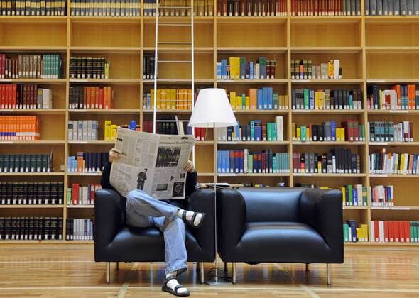 Zeitungsleser Zeitung Bibliothek Donnerstag (25.10.12), Weimar, Studienzentrum der Herzogin Anna Amalia Bibliothek Bücherkubus: Ein Mann sitzt in einem Sessel vor Bücherregalen und liest die Tageszeitung International Herald Tribune .