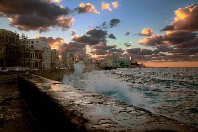 Kuba, Havanna Centro. Sonnenuntergang am Malecon (Malec—n) , die Sonne faerbt den Himmel rot und beleuchtet die Wolken. Die Brandung schlaegt ueber die Mauern des Malec—n.