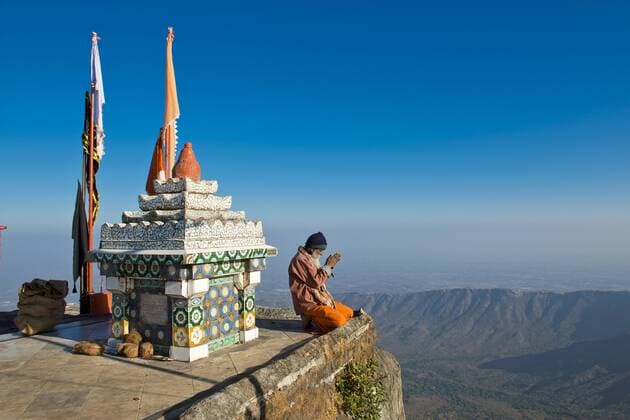  Ein heiliger Mann oder Sadhu sitzt mit gefalteten Händen ins Gebet vertieft am Abgrund vor einem hinduistischen Tempelschrein mit Gebetsfahnen iblwgb03062331.jpg