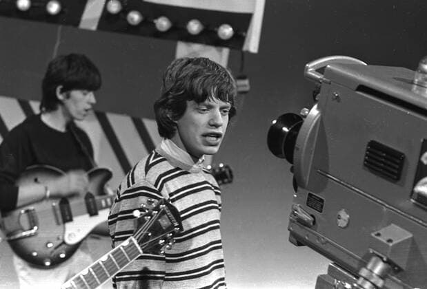 Mick Jagger , lead singer of the Rolling Stones , singing to a television camera during a performance on a TV pop show . Keith Richards is playing behind him . 1960s, Fernsehen, Fernsehshow, Fernsehstar, Fernseher, 1960er, 60er Jahre UnitedArchives00152771 