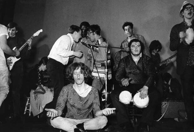 Hippy meditating at a musical event with people playing tambourines and bongo drums and singing. UnitedArchives00203008 