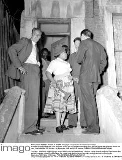 A woman stands outside her front door with an axe wih her husband behind the door after her house was attacked during the race riots in Notting Hill, London. 1st September 1958 UnitedArchives00579765 