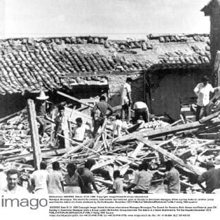 Managua, Nicaragua: The search for remains, both human and material, goes on Sunday in downtown Managua. While a group looks on, another group searches the debris of a home shattered by the Earthquake. December 1972  UnitedArchives01031360