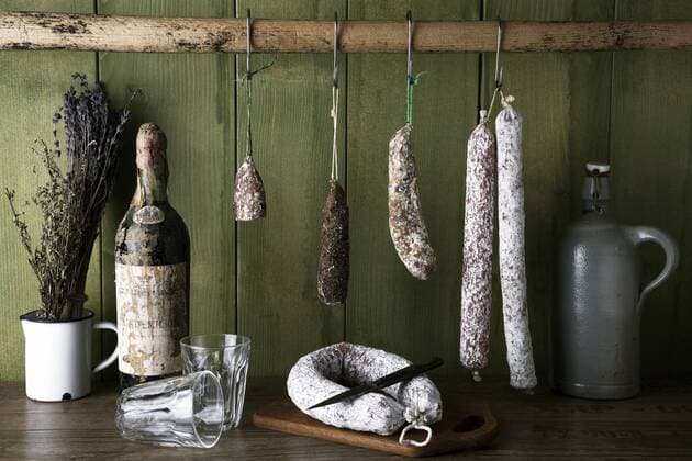 Verschiedene Sorten Salami hängen vor einer grünen Holzwand ibljwt03797448.jpg