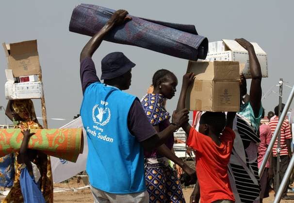 (131229) -- KHARTOUM, Dec. 29, 2013 (Xinhua) -- A staff of the WFP (United Nations World Food Programme) helps the South Sudanese refugees carry relief materials in a UN camp in Juba, capital of South Sudan, Dec. 29, 2013. According to the UN, the fighting has led to well over a thousand deaths and the displacement of at least 122,000 people, some 63,000 of whom have taken refuge in UN bases in the country. (Xinhua Lv Rui) SOUTH SUDAN-JUBA-UN-REFUGEES 