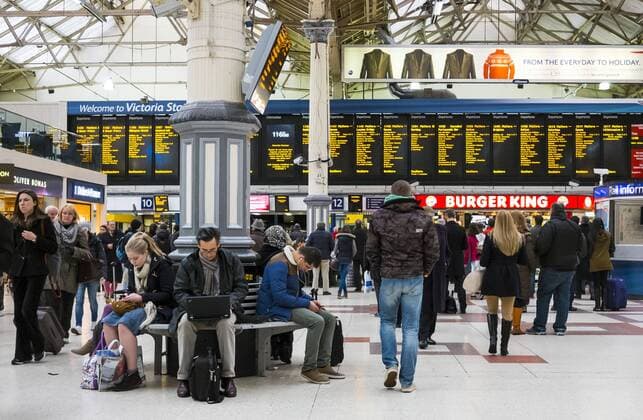 Passagiere und Touristen warten an der Anzeigetafel am Bahnhof Victoria Station mit Burger King Fast Food Restaurant in London, England, Uk, Grossbritannien am 14.11.2013. Ein Mann arbeitet am Notebook Computer.