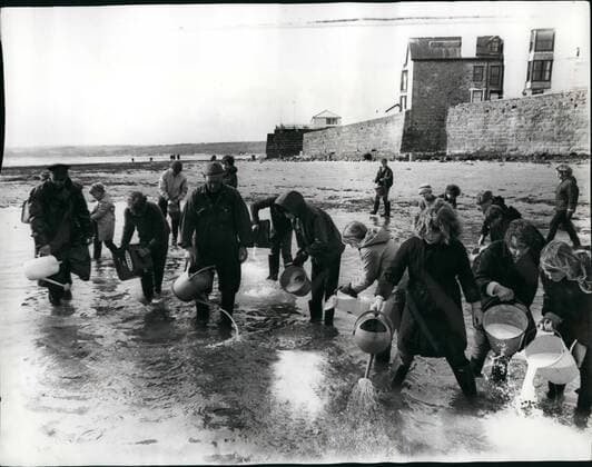 Mar. 03, 1967 - Vast oil threat to the South Coast - Volunteers help to clean the beaches in Cornwall. The wrecked oil tanker Torrey Canyon, pounded by the heavy seas, has now broken into three parts and sinking rapidly. Half of the ship s 120,000-ton cargo of thick black oil has poured into the sea and is being driven slowly up the English Channel - menacing the whole South Coast. Yesterday local Cornish housewives and their children, armed with buckets and watering cans were spraying the beach at Marazion, Cornwell,with detergent to was away the oil that coated their golden sands. Photo Shows Fighting the oil menace at Marazion, Cornwall, these local children were out in force spraying the oil with detergent using watering cans and buckets.  - ZUMAk09