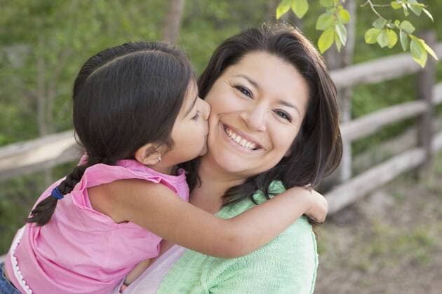 A mother in the park with her daughter, laughing and kissing each other. 