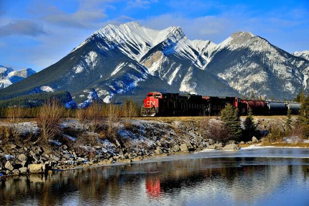 A Canadian National freight train passing a snow-capped rocky mountain on the main rail line through Jasper National Park in Alberta, Canada.  acp66540