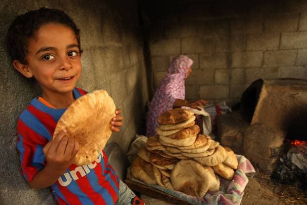 A Palestinian child holds bread, while Samia AL-najar, age 42 (R), bake bread on an old clay oven near her destroyed house in Khan Younis that was destroyed by an Israeli air strike during a seven-week war with Gaza, in the southern Gaza Strip on September 21, 2014.Palestinian families made homeless during the latest war between Israel and Gaza, in Khan Yunis Khuzaa neighbourhood in the southern Gaza Strip. According to the UN agency for aid to Palestinian refugees (UNRWA), 65,000 homeless Palestinians are still sheltering in UN schools awaiting accommodation and thousands more have sought refuge with relatives.  GAZ2014092113