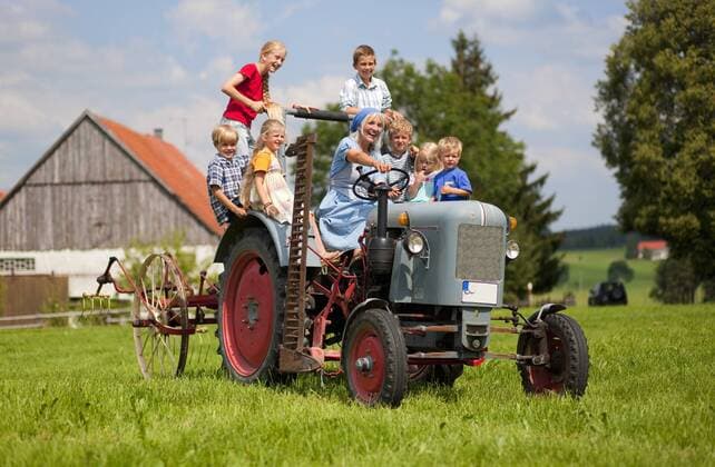 Germany, Bavaria, Woman with group of children sitting on old tractor in front of farmhouse model released property released  HSIYF000039