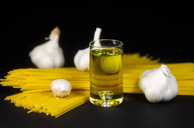 Glass of olive oil with spaghetti and garlics on black bakground, close up  JTF000415