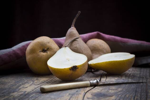Sliced and whole pears (Pyrus), a knife and a kitchen towel on wooden table  LVF000646