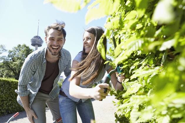 Germany, Cologne, Young couple cutting leaves with shears, smiling model released property released  RHYF000442