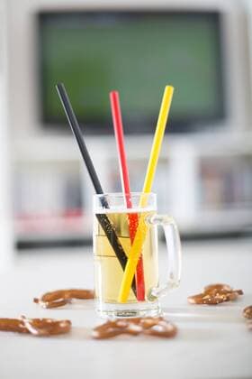 Beer mug with three drinking straws in German national colours and pretzels in front of television with empty soccer field  SARF000667