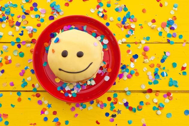 Geburtstag - Symbolbilder Krapfen mit lustigem Smiley Gesicht mit buntem Konfetti  1079701748