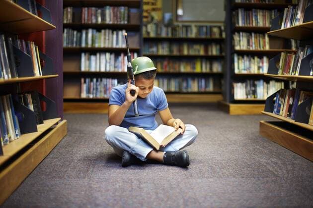 Boy with helmet and gun reading book in library model released Symbolfoto property released  ZEF000195