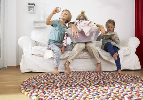 IMAGO Creative: Internationaler Frauentag, Mental Load und Care-Arbeit Exhausted mother with laundry basket on couch with children using digital tablet and cell phone model released Symbolfoto property released  FSF000270
