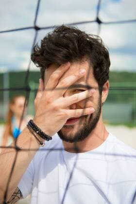Young man covering his face at net of beach volleyball field model released Symbolfoto  WESTF020679