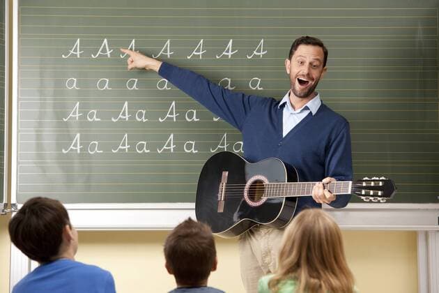 IMAGO Creative: Bildung, Musikerziehung Teacher with guitar at blackboard showing variations of letter A model released Symbolfoto property released  MFRF000110