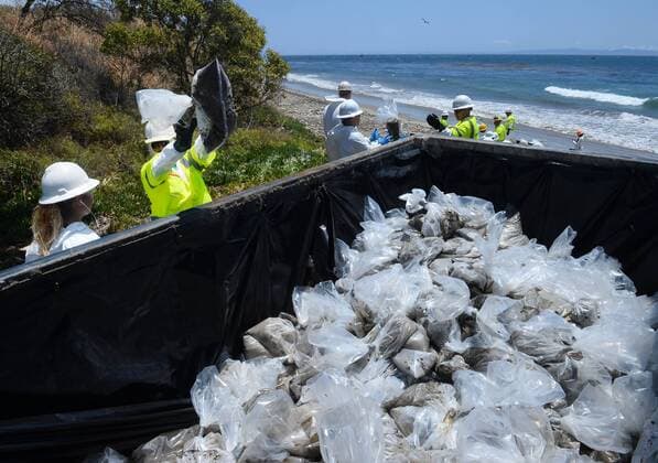 Workers form an assembly line to place bags of sand contaminated by oil in a dumpster for disposal along Refugio Beach as efforts continue to remove the oil that has spilled an estimated 100,000 gallons off the Santa Barbara County coast in Goleta, California on May 22, 2015. A unified command center established for the spill said the worst-case estimate is that 2,500 barrels of oil was released from a pipeline operated by Plains All American. Sheen is spread several miles from the site of the spill off the coast of Refugio State Beach.  LAP2015052212 JIMxRUYMEN