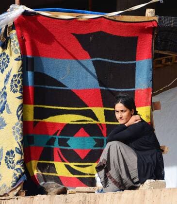 TOKYO, Japan - A refugee woman sits in front of a makeshift room made by attaching cloth to pillars on Dec. 9, 2014, at an unfinished building in northern Iraq where she and others fleeing attacks by Islamic State extremists are sheltered. Many refugees face intense cold weather without adequate warm clothing and other winter supplies.  0106036