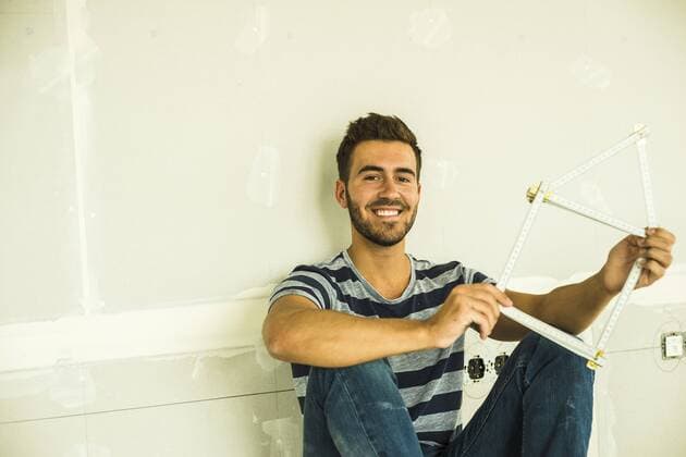 Smiling young man sitting at blank wall holding pocket rule model released Symbolfoto  UUF004186